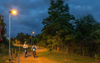 Zwei Radfahrer fahren nachts auf einem von LED-Leuchten erhellten Radweg