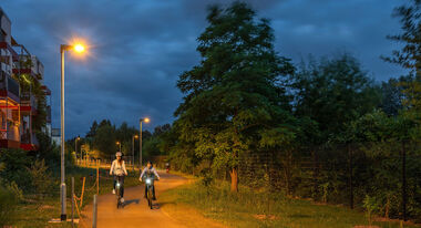 Zwei Radfahrer fahren nachts auf einem von LED-Leuchten erhellten Radweg