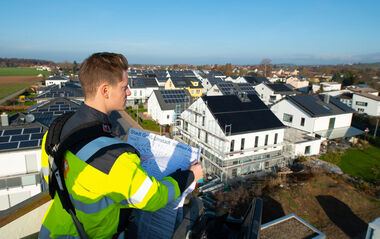 e-netz-Mitarbeiter hält einen Bebauungsplan in der Hand und blickt auf Neubauten der Solarsiedlung in Groß-Umstadt