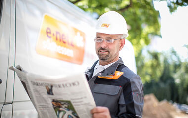 e-netz-Monteur steht vor einem Montagefahrzeug und liest die Tageszeitung Darmstädter Echo