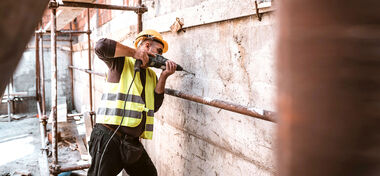Bauarbeiter bohrt mit einer Bohrmaschine ein Loch in eine Betonmauer