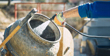 Auf einer Baustelle wird Wasser über einen Schlauch in einen Betonmischer gespritzt